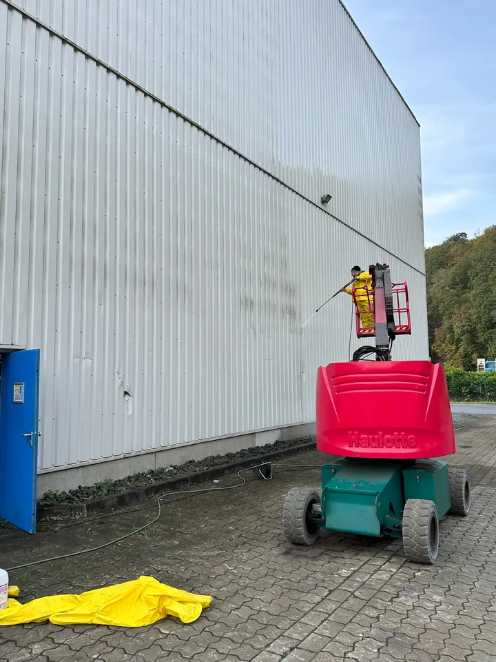 Fassadenreinigung mit Hubarbeitsbühne: Mitarbeiter reinigt die Blechfassade einer Halle mit Hochdruck