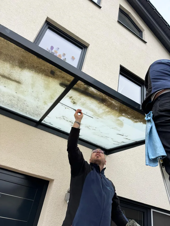 Reinigung eines Glasvordachs: der Grünbelag wird mit dem Abzieher entfernt