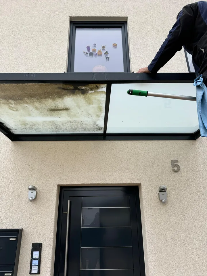 Glasvordach über einer Haustür während der Reinigung — linke Hälfte noch stark verschmutzt, rechte Hälfte bereits sauber